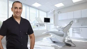 ד"ר ערן פרמון מחייך במרפאה מודרנית, כיסא דנטלי וציוד
